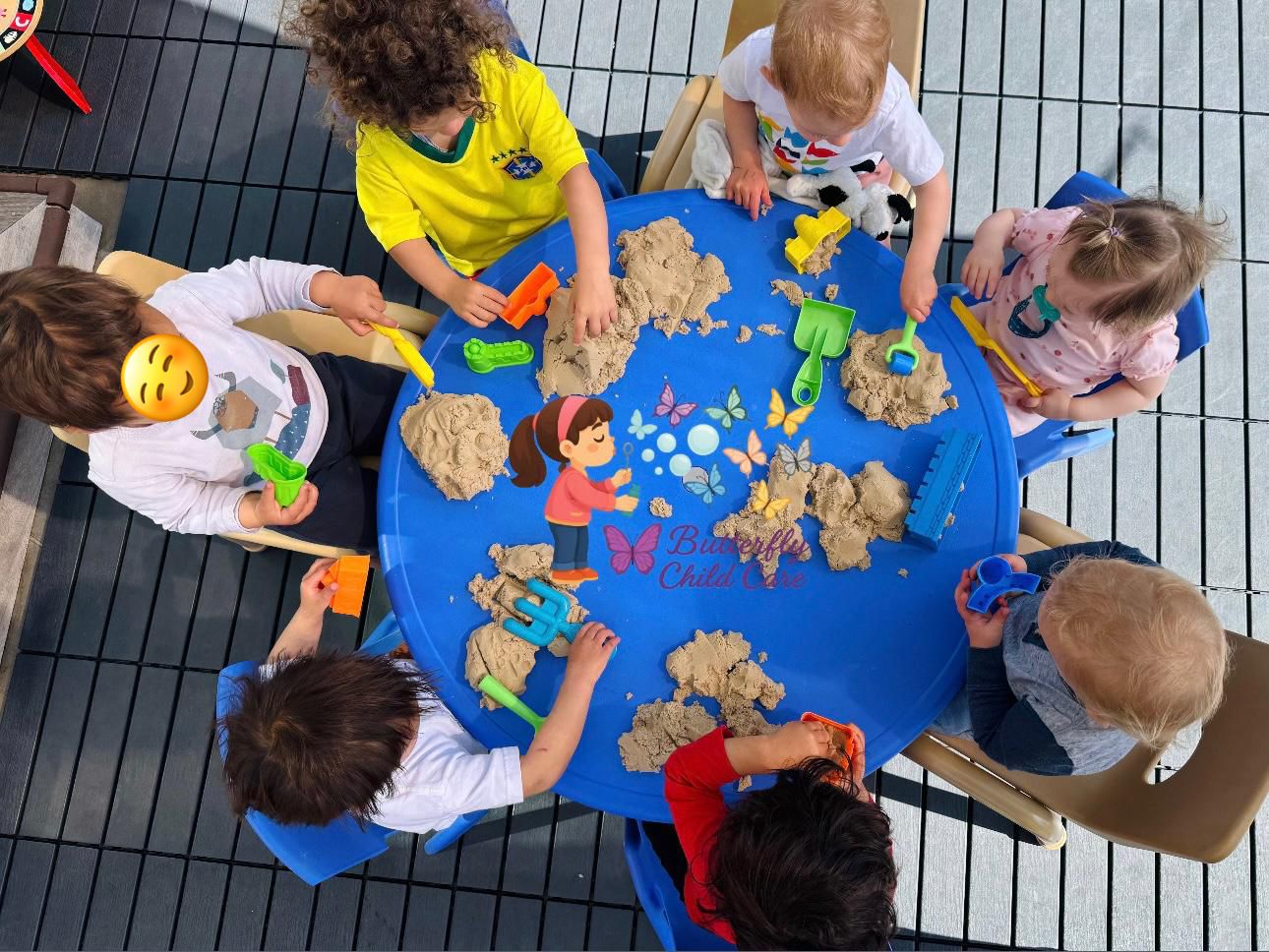 Children engaged in sensory sand play at a blue table at Butterfly Child Care